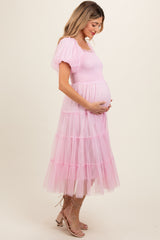woman wearing a pink tiered tulle maternity dress and holding her baby bump