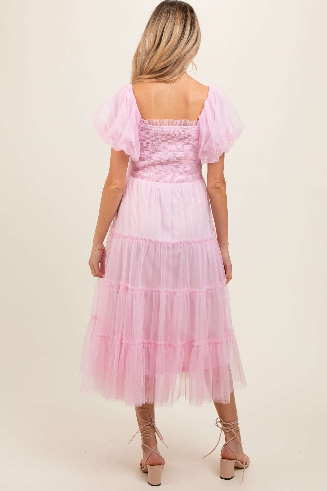 woman wearing a pink maternity dress with puff sleeves and a tiered tulle skirt, showing a baby bump from the back