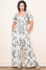 woman wearing a cream floral print jumpsuit with puff sleeves and side pockets