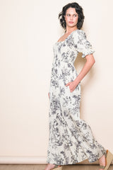 woman wearing a white floral maxi dress with puff sleeves and side pockets, posing sideways against a light background