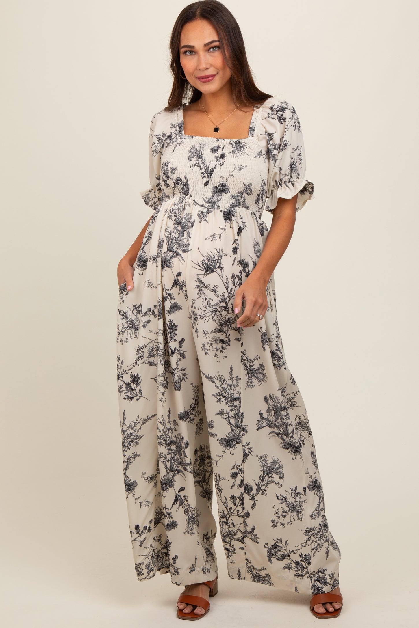 woman wearing a beige floral print maternity jumpsuit with smocked bodice and flowy wide legs, showcasing her baby bump