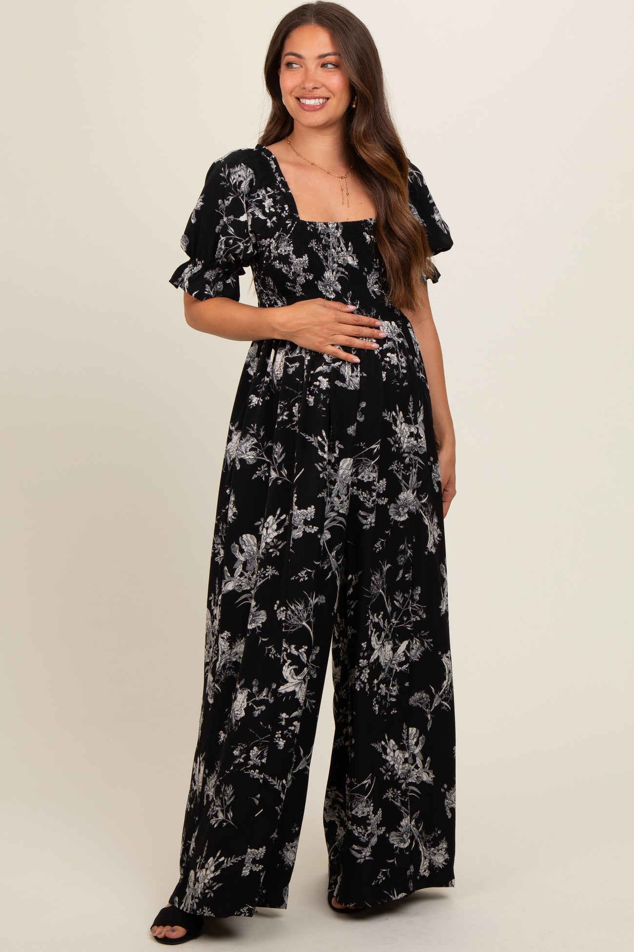 woman wearing a black floral print maternity jumpsuit and showing her baby bump