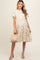 woman wearing a beige floral maternity dress with short sleeves and a tiered skirt, holding a woven bag