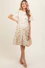 woman wearing a floral print beige maternity dress with short sleeves and a tiered skirt, holding a woven bag