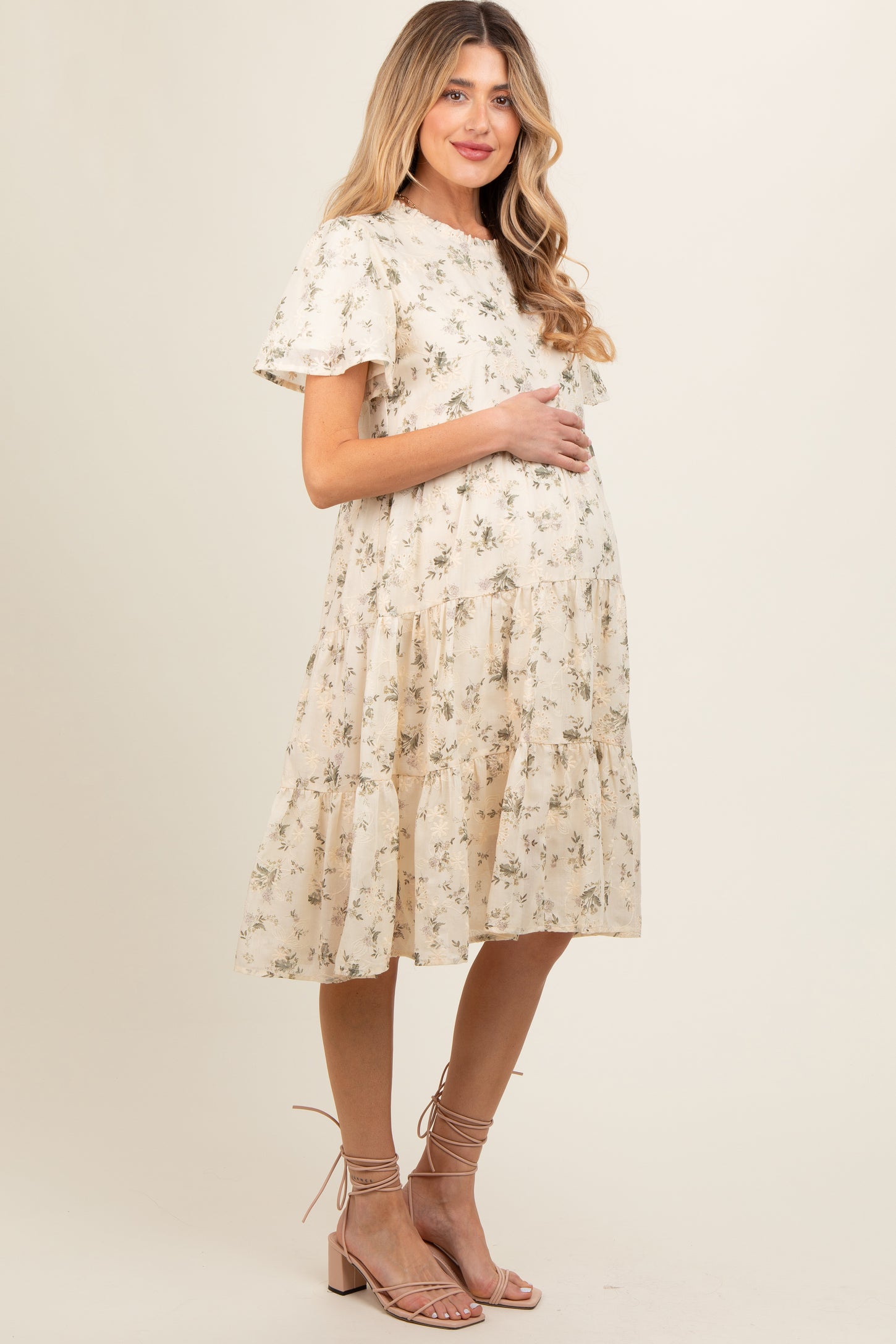 woman wearing a cream floral print maternity dress with short sleeves and a tiered skirt, holding her baby bump