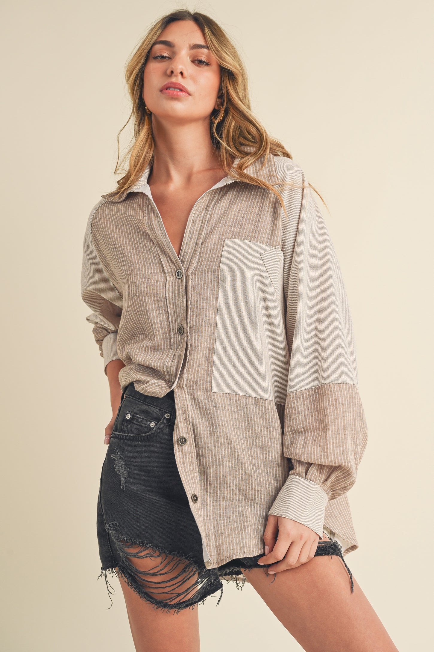 woman wearing a beige and cream striped button-up shirt with a front pocket and distressed black shorts