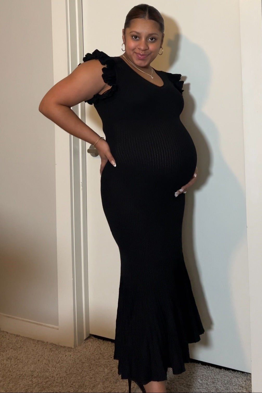 woman wearing a black ribbed maternity dress with ruffle sleeves and a fitted silhouette, showcasing her baby bump