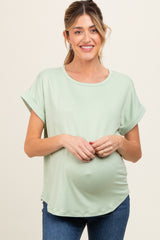 woman wearing a light green maternity top with rolled sleeves and a visible baby bump