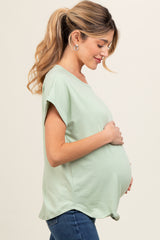 woman wearing a light green maternity top and holding her baby bump