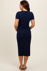 woman wearing a navy blue short sleeve maternity dress, fitted style, showing side ruching and knee-length hem