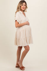 woman wearing a light beige maternity dress with a tiered skirt and short sleeves, holding her baby bump