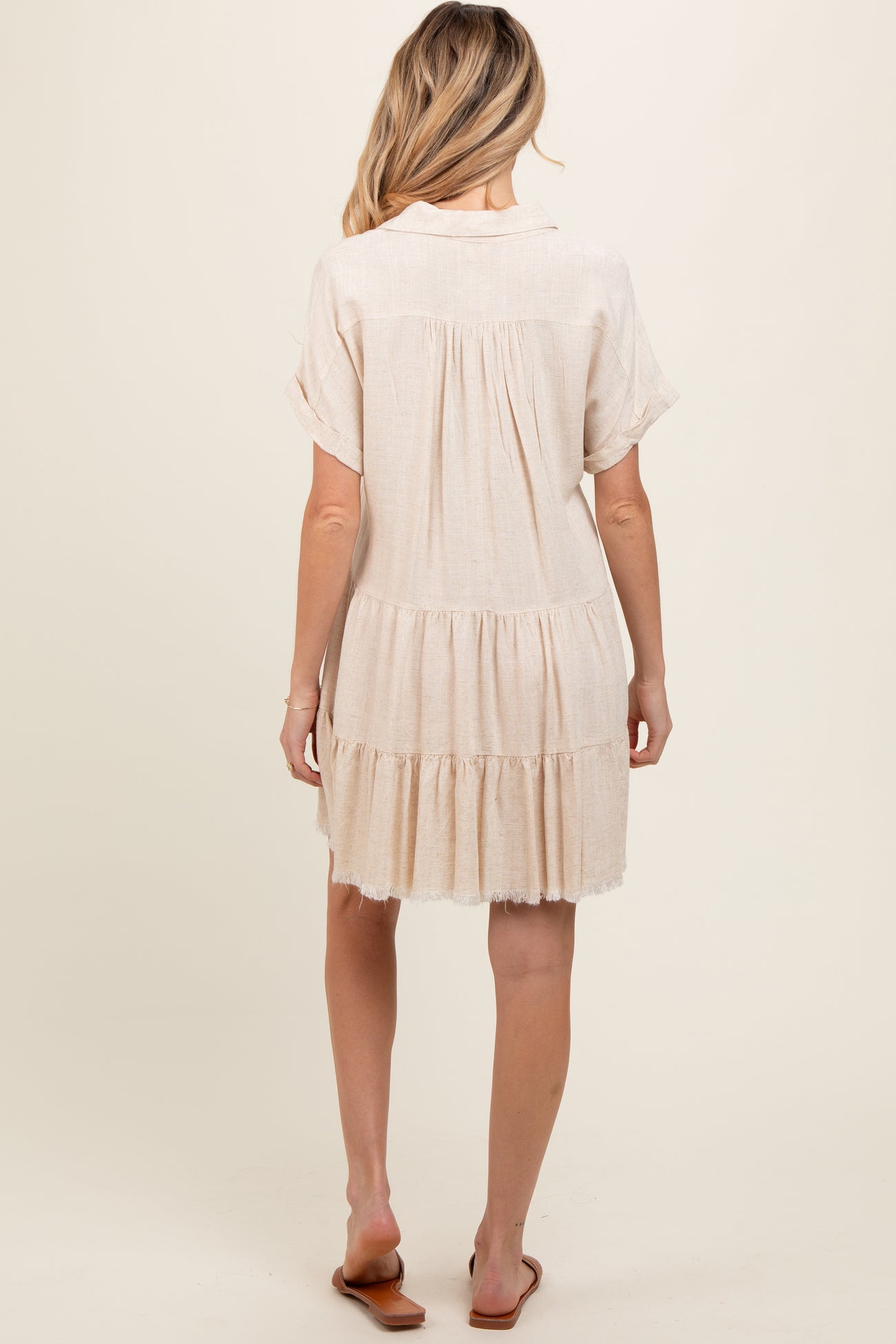 woman wearing a light beige maternity dress with short sleeves and tiered ruffles, shown from the back