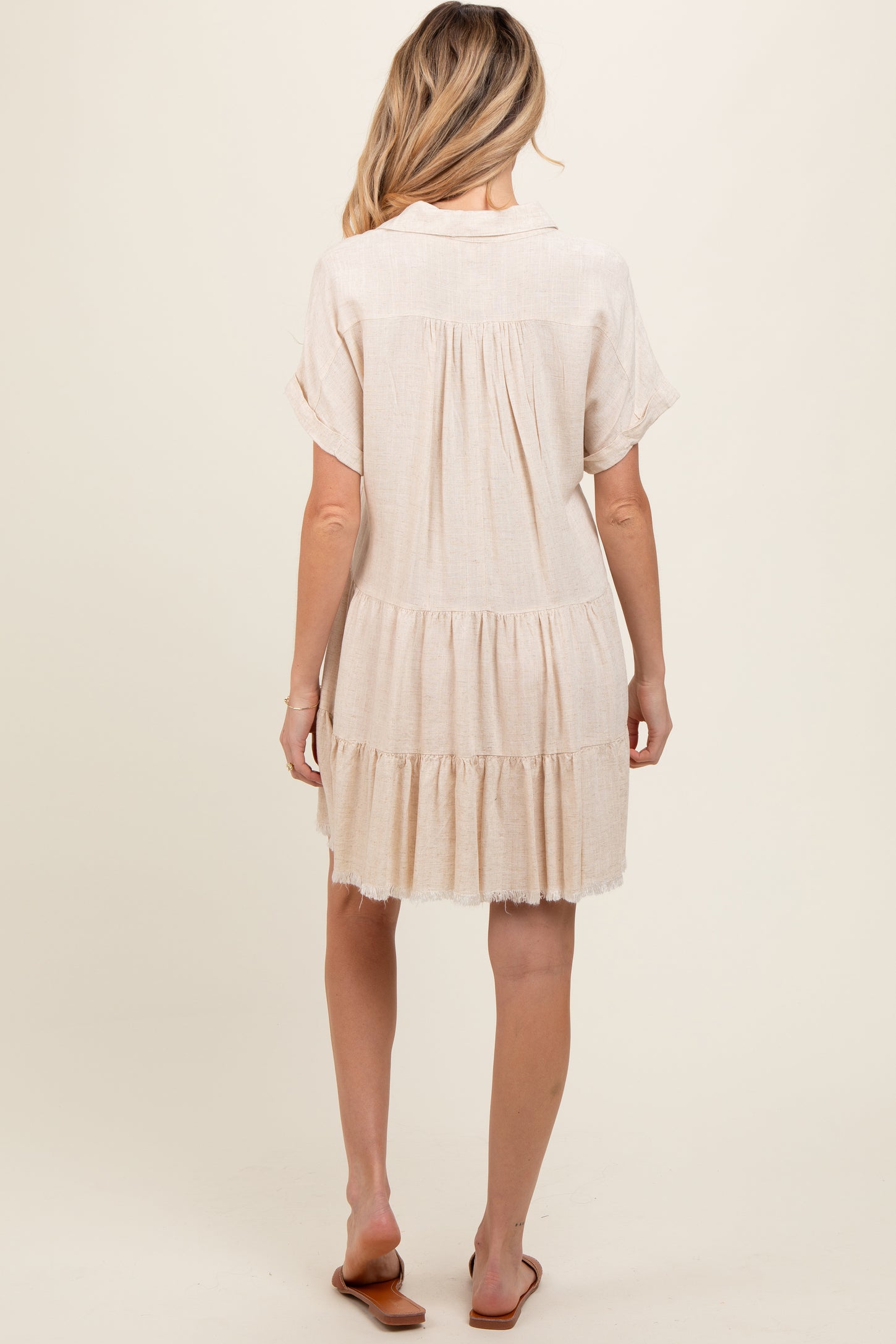 woman wearing a light beige maternity dress with short sleeves and tiered ruffles, shown from the back