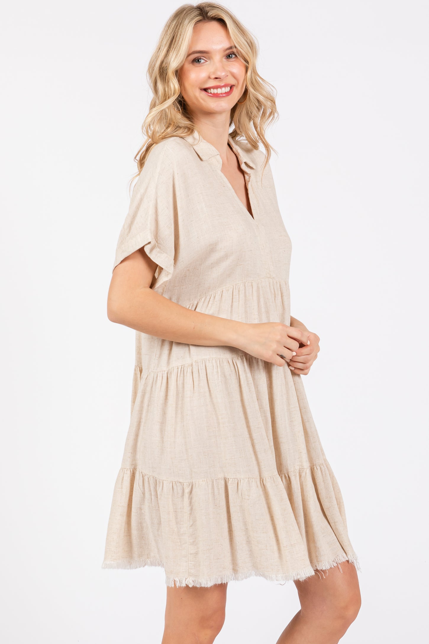 woman wearing a light beige short sleeve tiered dress with a v-neck and fringe hem