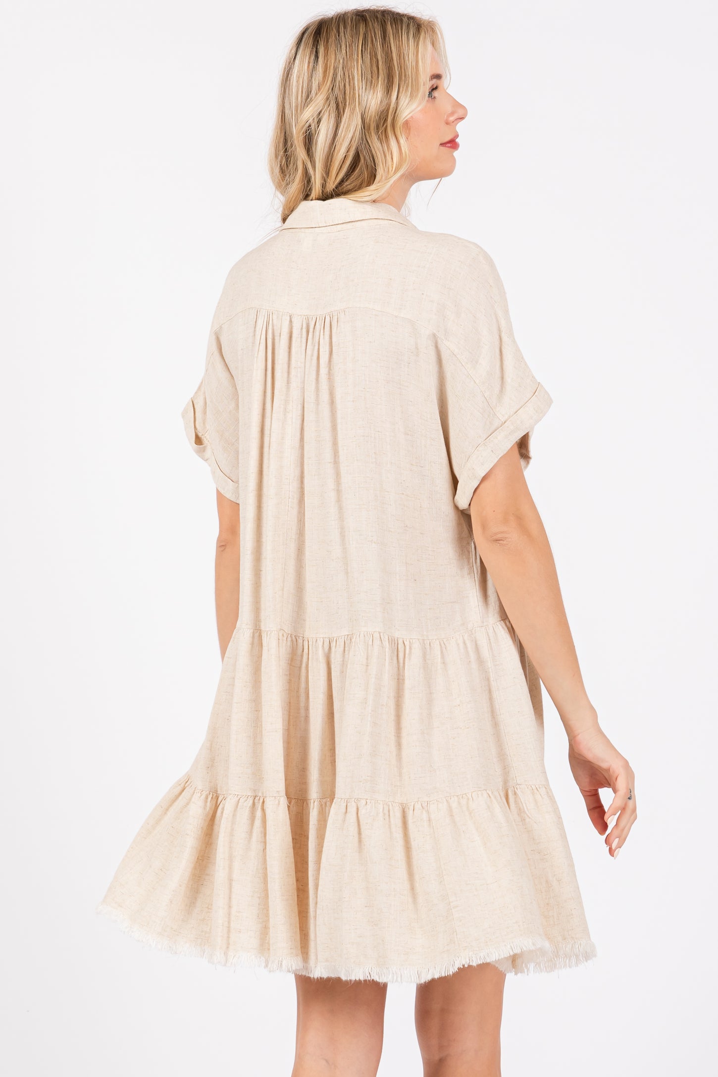 woman wearing a beige short sleeve tiered dress with a relaxed fit and frayed hem