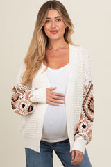 woman wearing a cream open knit maternity cardigan with patterned sleeves and holding her baby bump