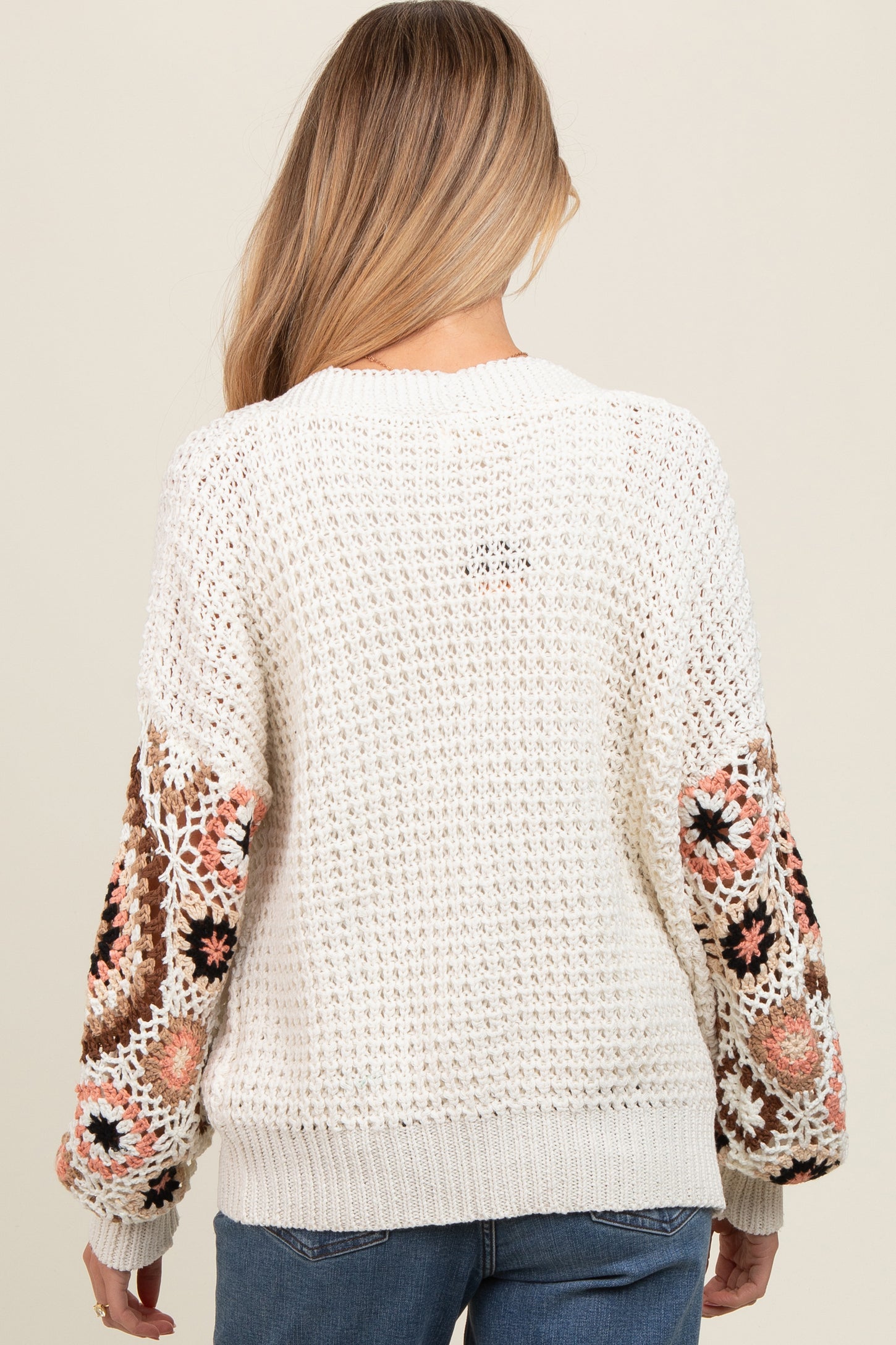 woman wearing a cream crochet maternity sweater with colorful floral embroidery on the sleeves
