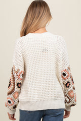 woman wearing a cream crochet maternity sweater with colorful floral embroidery on the sleeves