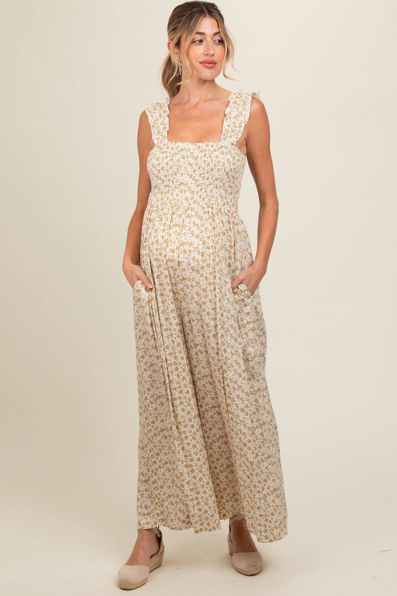 woman wearing a sleeveless floral print maternity maxi dress with ruffle straps and side pockets, displaying her baby bump