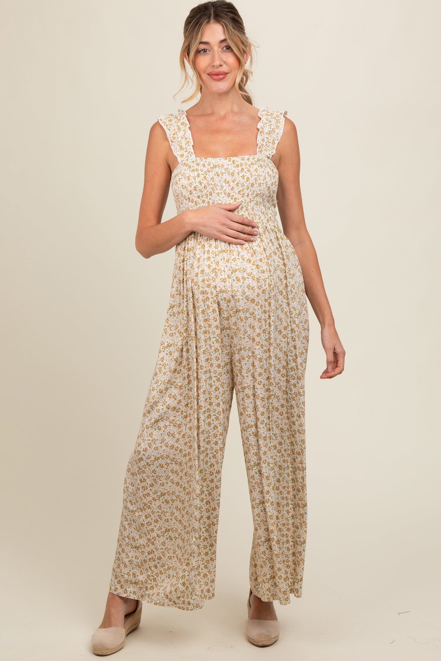woman wearing a floral print maternity jumpsuit with ruffled straps and holding her baby bump