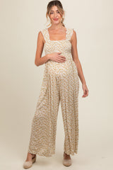 woman wearing a floral print maternity jumpsuit with ruffled straps and holding her baby bump