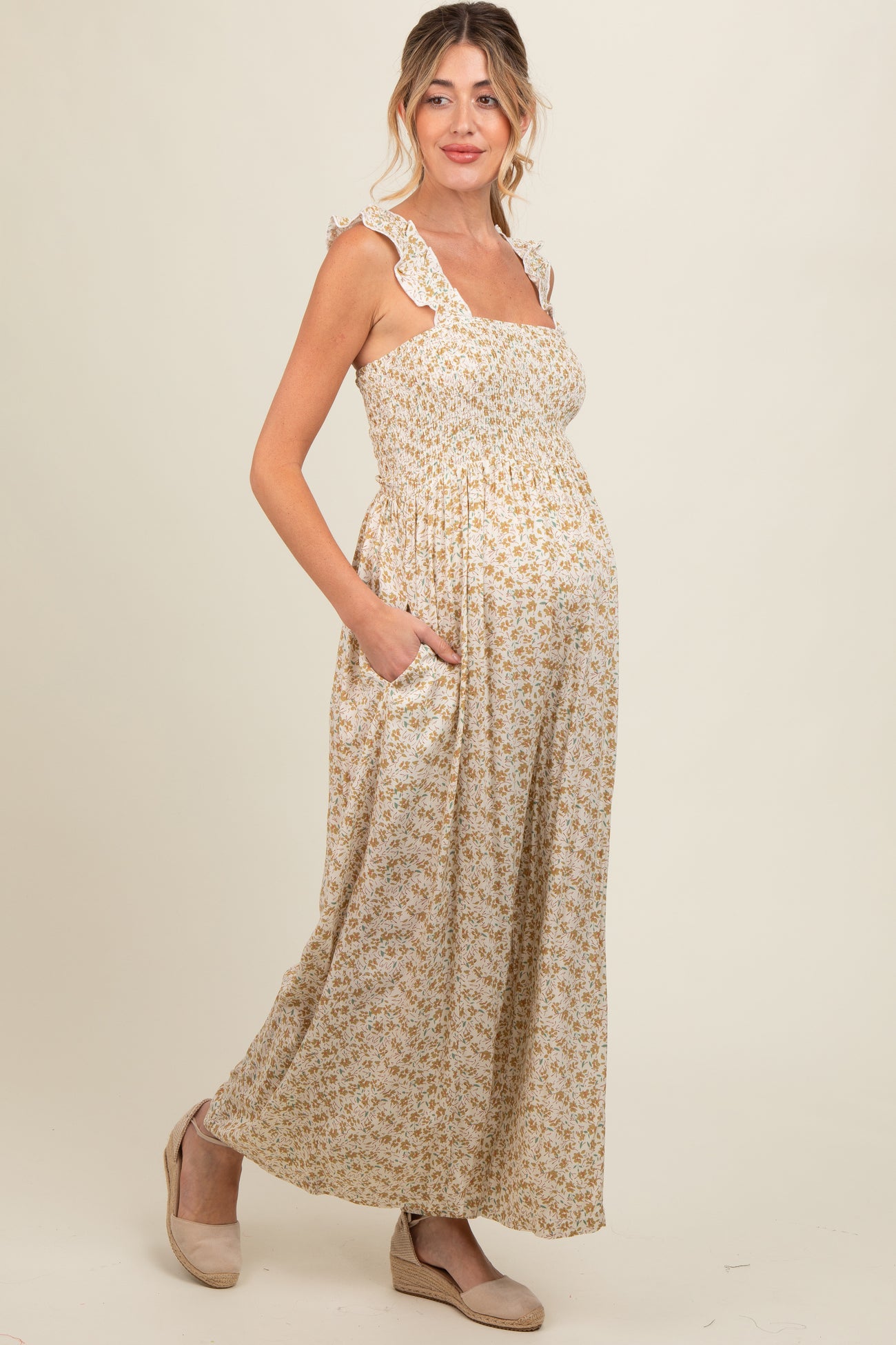 woman wearing a floral print maternity maxi dress with ruffle straps and pockets, showcasing her baby bump