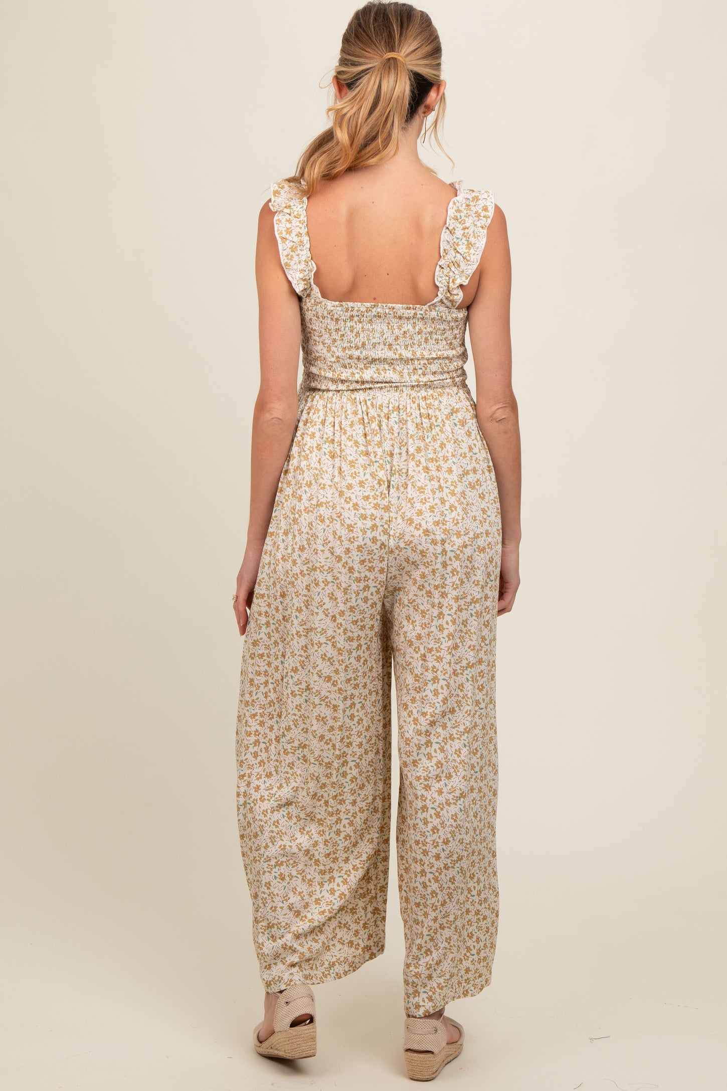 woman wearing a back view of a floral maternity jumpsuit with ruffled straps and wide legs