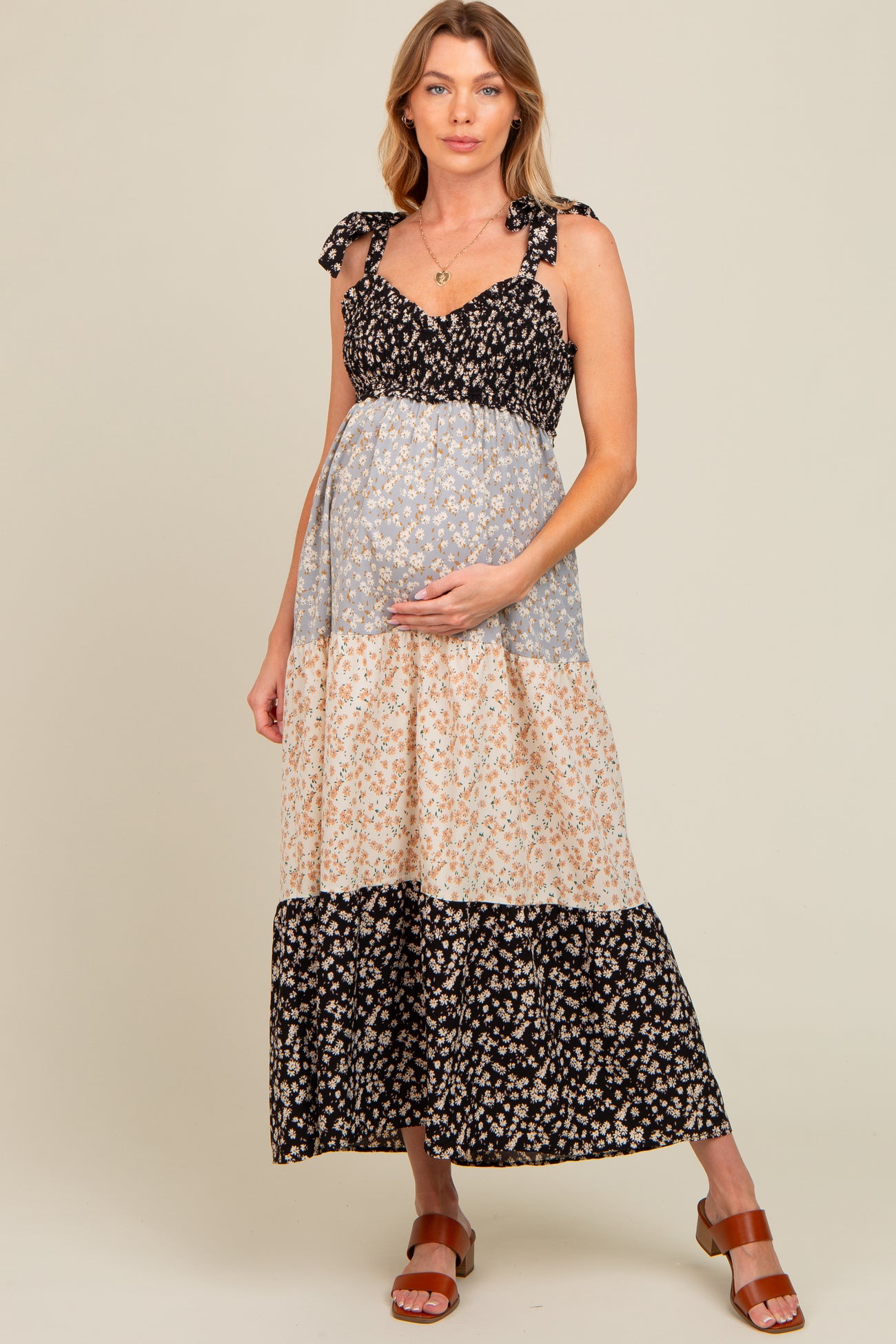 woman wearing a floral maternity maxi dress with tie straps and a baby bump, standing in a relaxed pose
