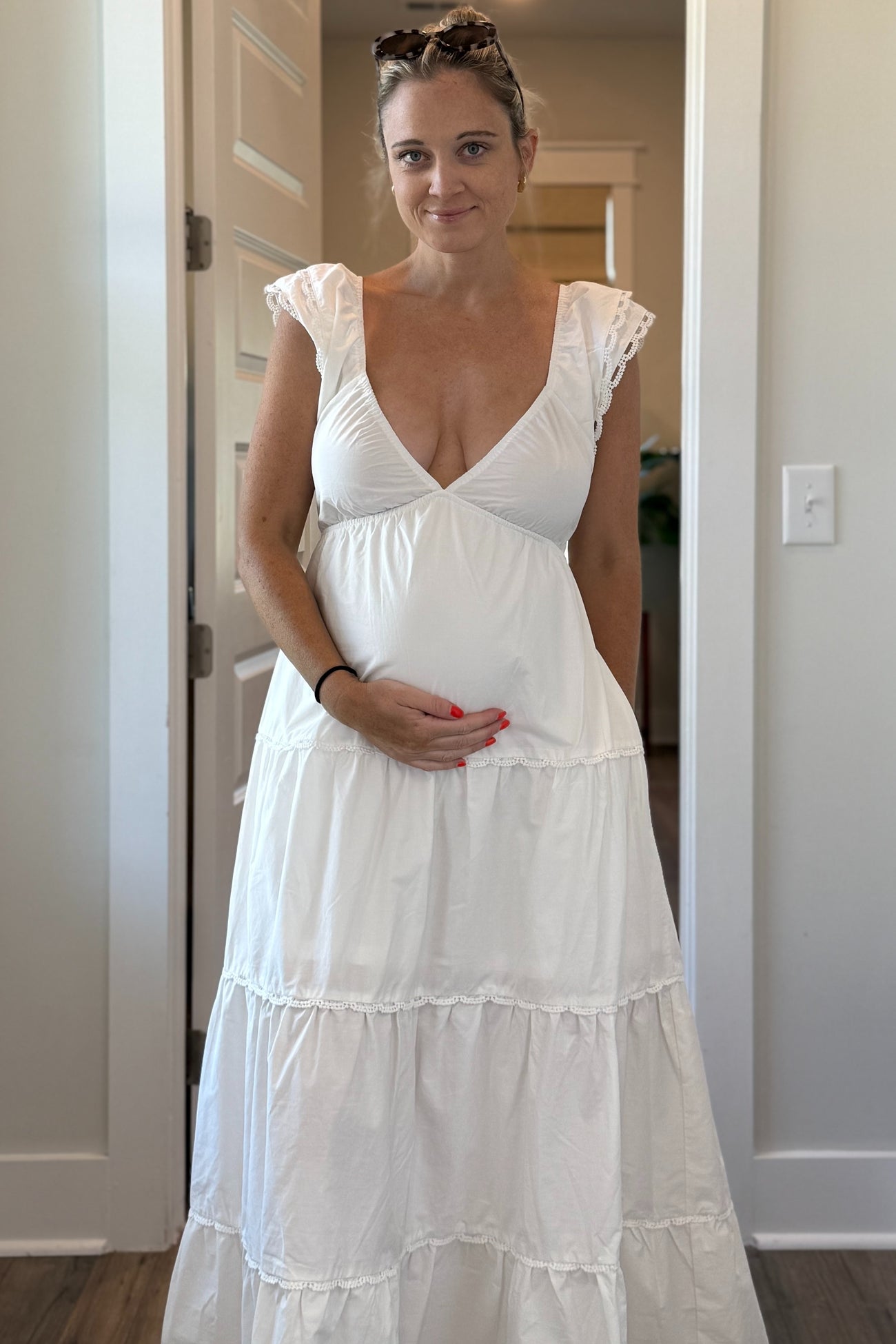 woman wearing a white maternity dress with a tiered skirt and puff sleeves, holding her baby bump