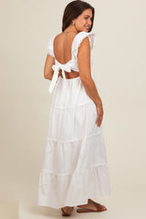 woman wearing a white maternity maxi dress with ruffle sleeves and a back tie detail, showing a baby bump