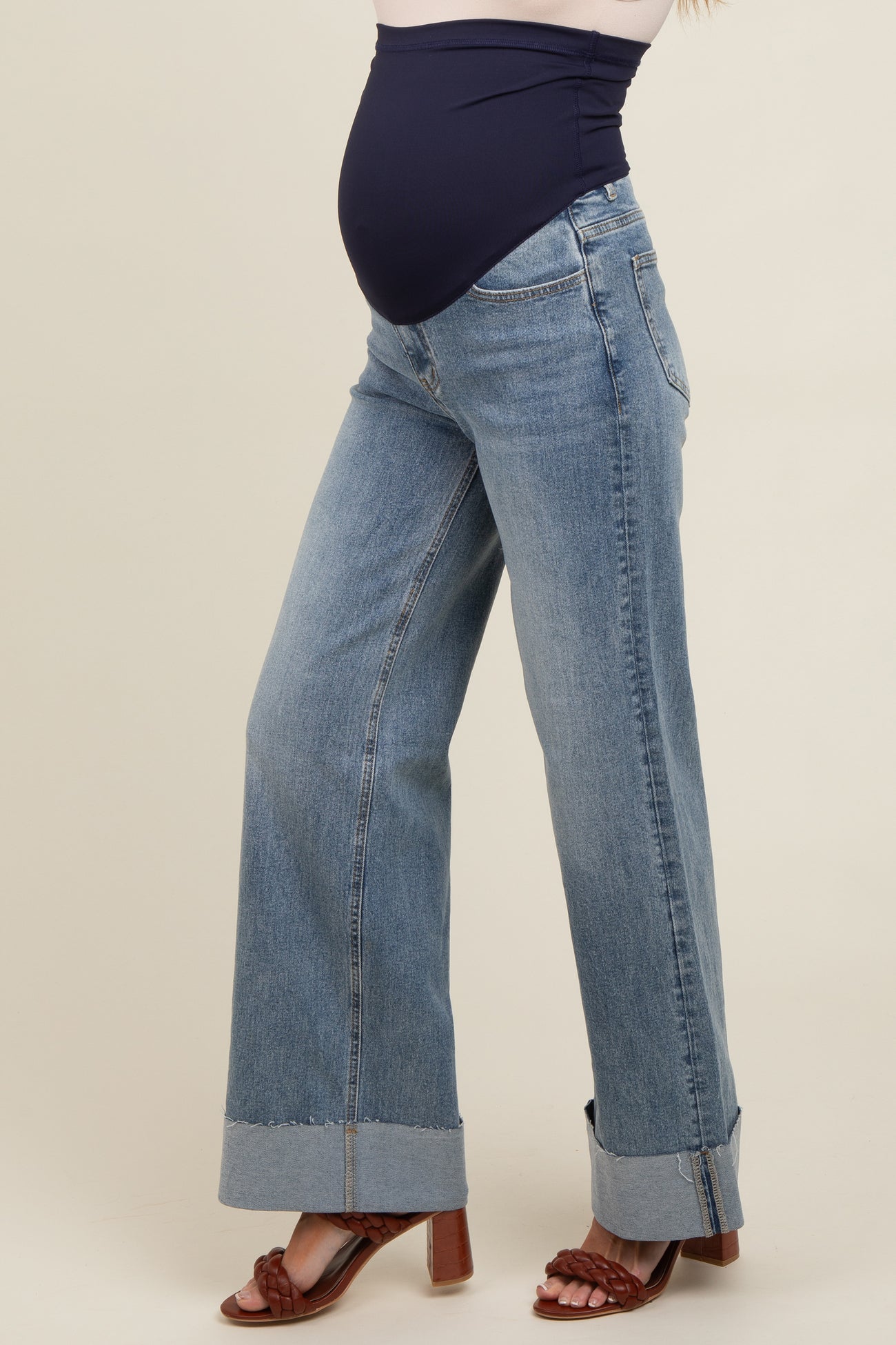 woman wearing a pair of light wash maternity jeans with a wide leg and a fitted navy blue maternity waistband, baby bump visible
