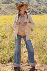 woman wearing a cream cardigan over a striped maternity top and flared jeans, displaying her baby bump in a field