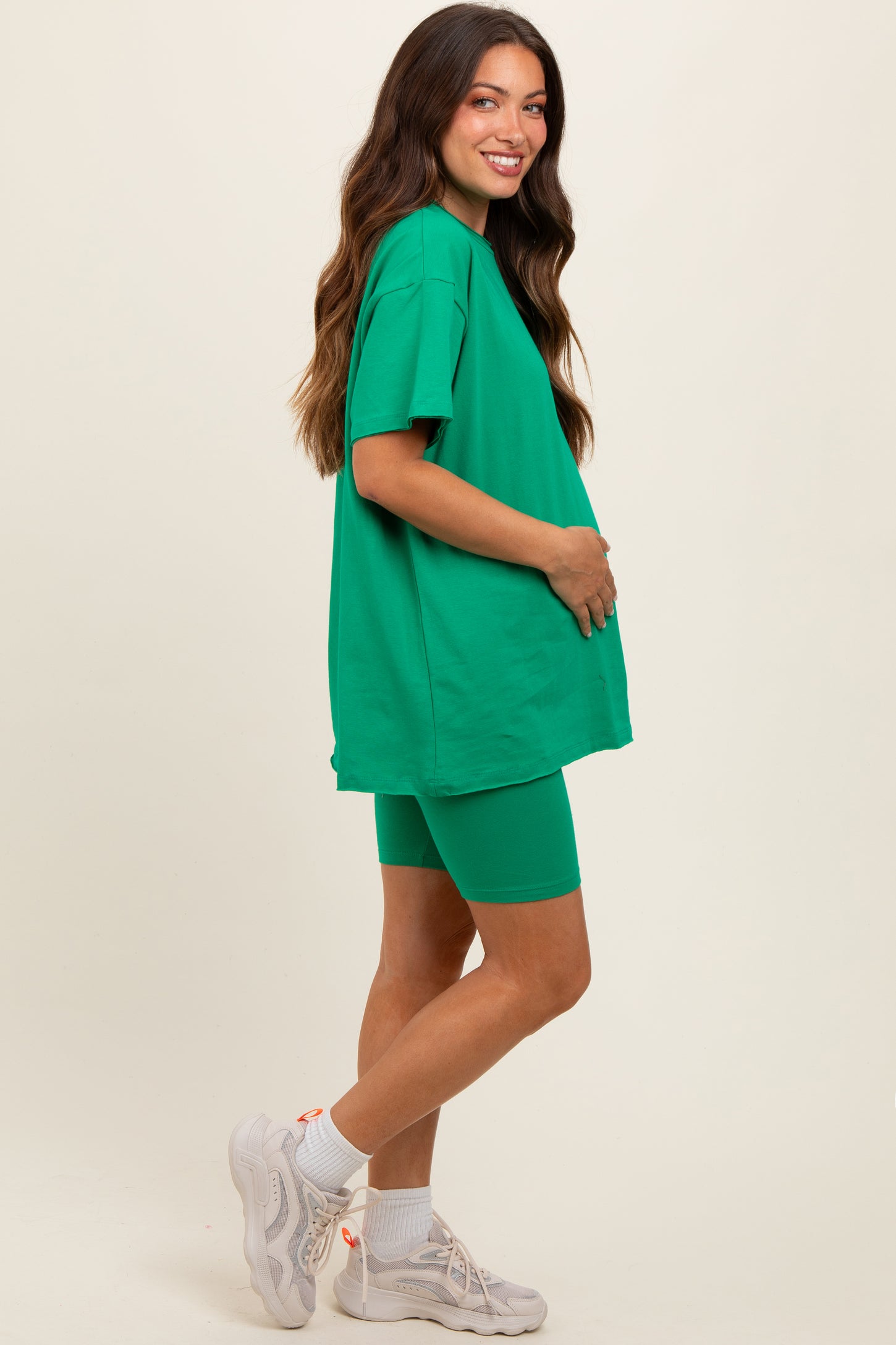woman wearing a bright green oversized t-shirt and matching bike shorts, showcasing her baby bump as maternity wear