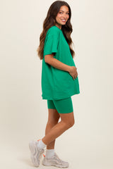 woman wearing a bright green oversized t-shirt and matching bike shorts, showcasing her baby bump as maternity wear