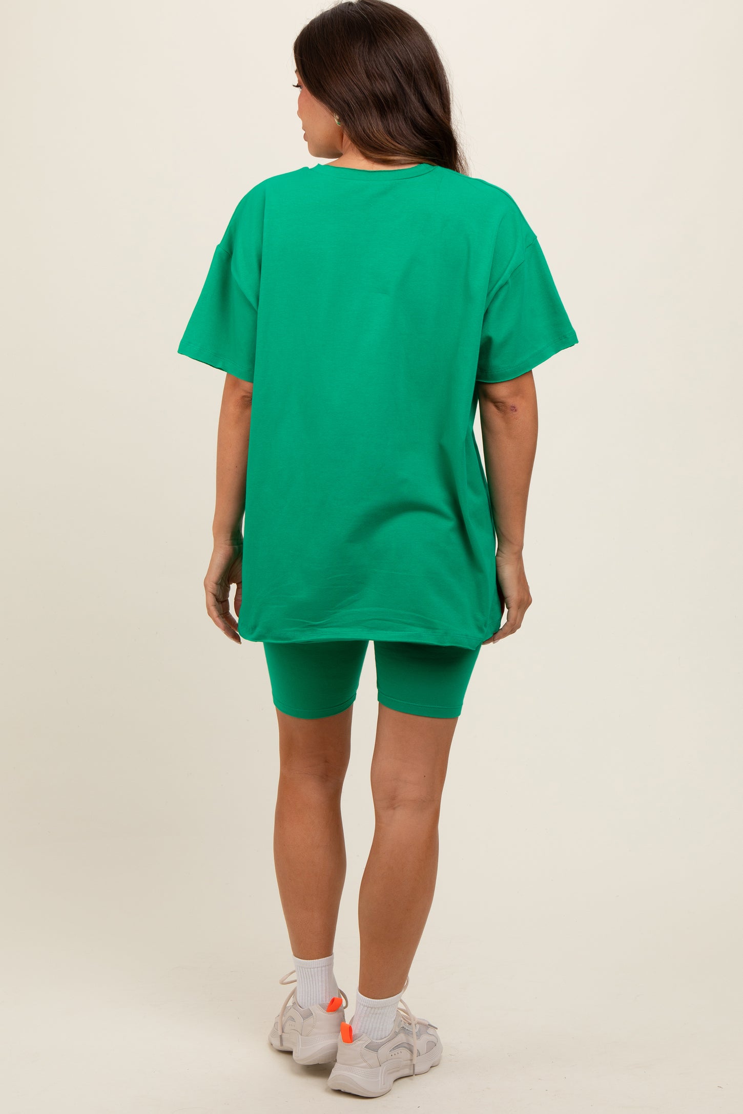 woman wearing a green oversized t-shirt and matching bike shorts, showcasing a casual maternity outfit