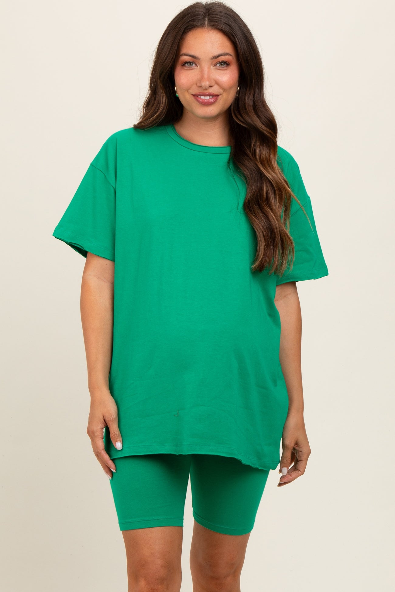 woman wearing a green oversized maternity t-shirt and matching bike shorts, with a visible baby bump