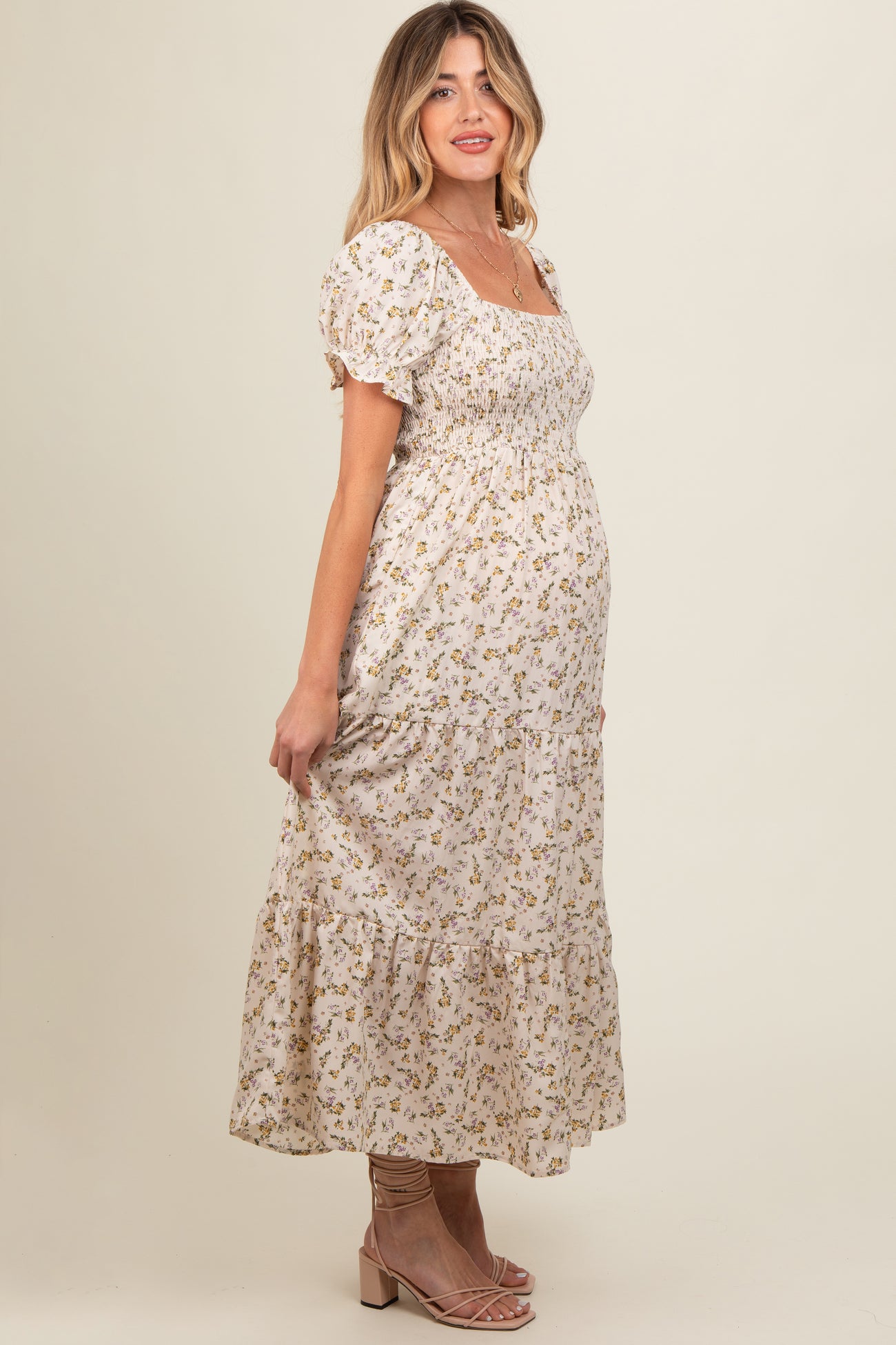 woman wearing a cream floral maternity maxi dress with puff sleeves and a fitted bodice, showing her baby bump