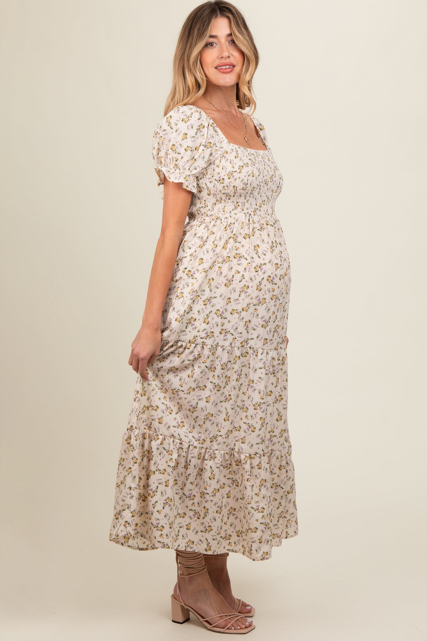 woman wearing a cream floral maternity maxi dress with puff sleeves and a fitted bodice, showing her baby bump