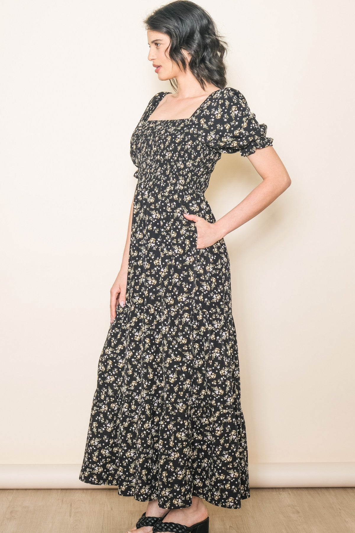 woman wearing a black floral maxi dress with puff sleeves and pockets, styled in a relaxed pose