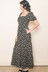 woman wearing a black floral maxi dress with puff sleeves and pockets, styled in a relaxed pose
