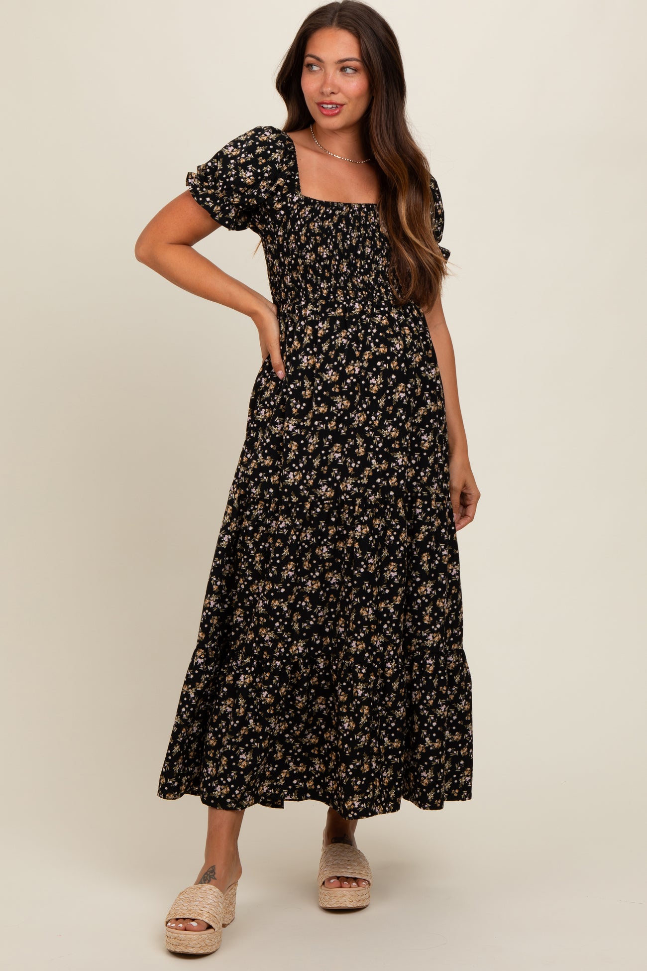 woman wearing a black floral maternity maxi dress with short puff sleeves and pockets, smiling and posing with her hand on her hip
