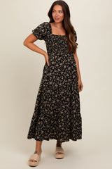 woman wearing a black floral maternity maxi dress with short puff sleeves and pockets, smiling and posing with her hand on her hip