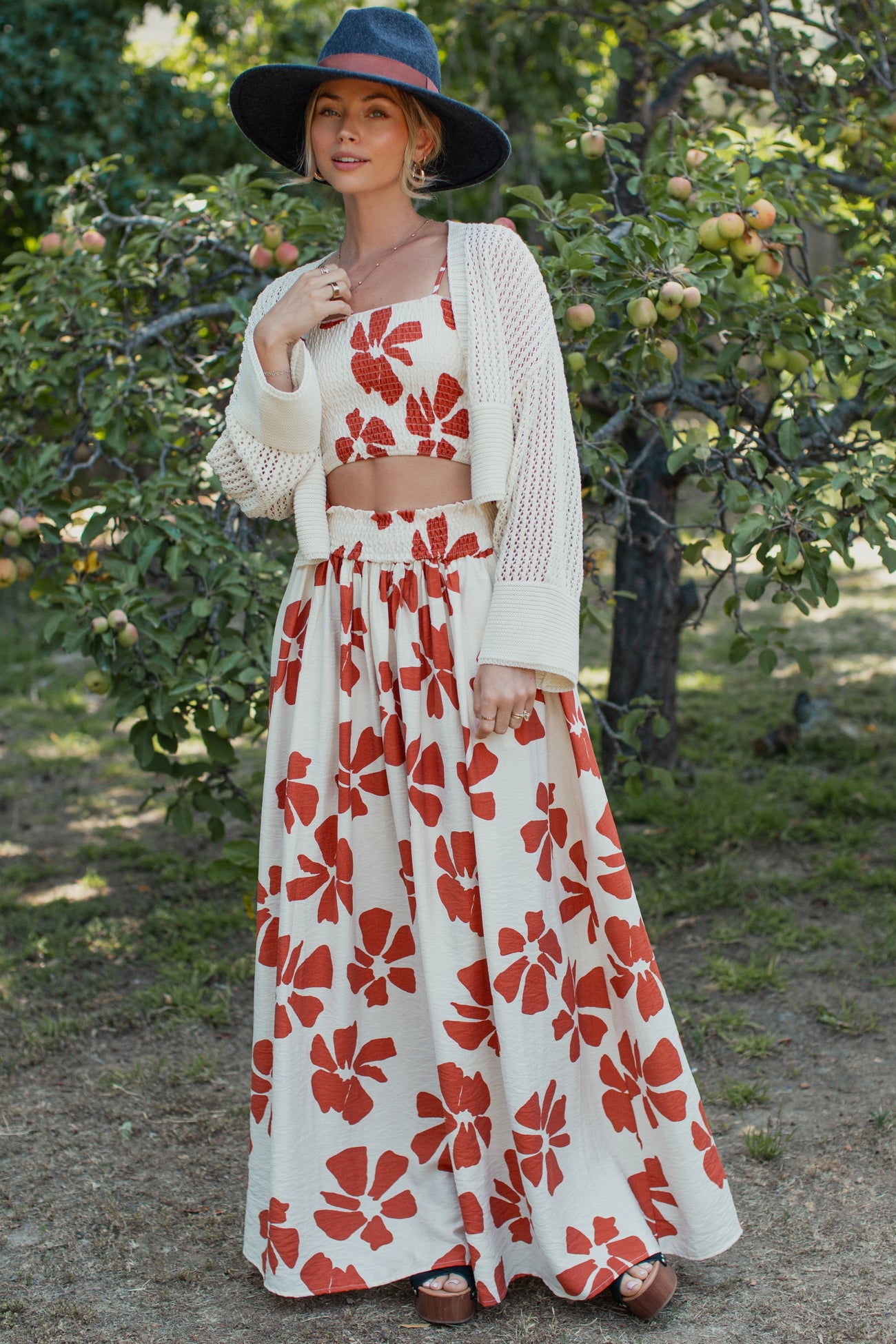 woman wearing a white floral maxi skirt and matching crop top with a knitted cardigan and wide-brimmed hat