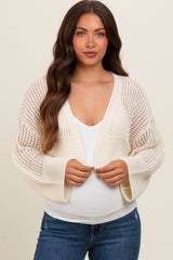 woman wearing a cream open-knit maternity cardigan over a white top and showing her baby bump