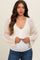 woman wearing a cream open-knit maternity cardigan over a white top and showing her baby bump