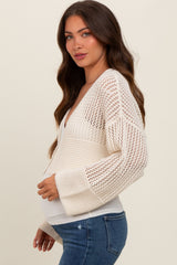 woman wearing a cream maternity cardigan with open knit design and bell sleeves, displaying her baby bump