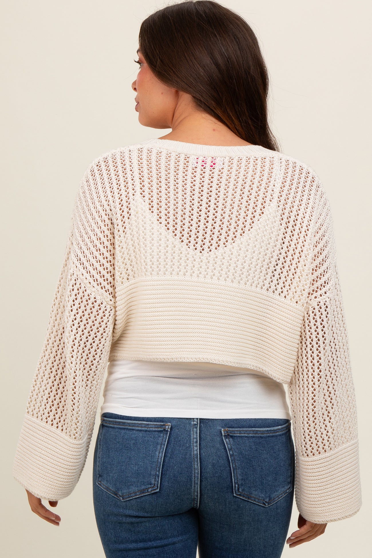 woman wearing a cream open knit maternity sweater with long sleeves, showing a relaxed fit and cropped style from the back