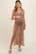 woman wearing a tan knitted maternity dress with a side slit, holding her baby bump and paired with casual sandals