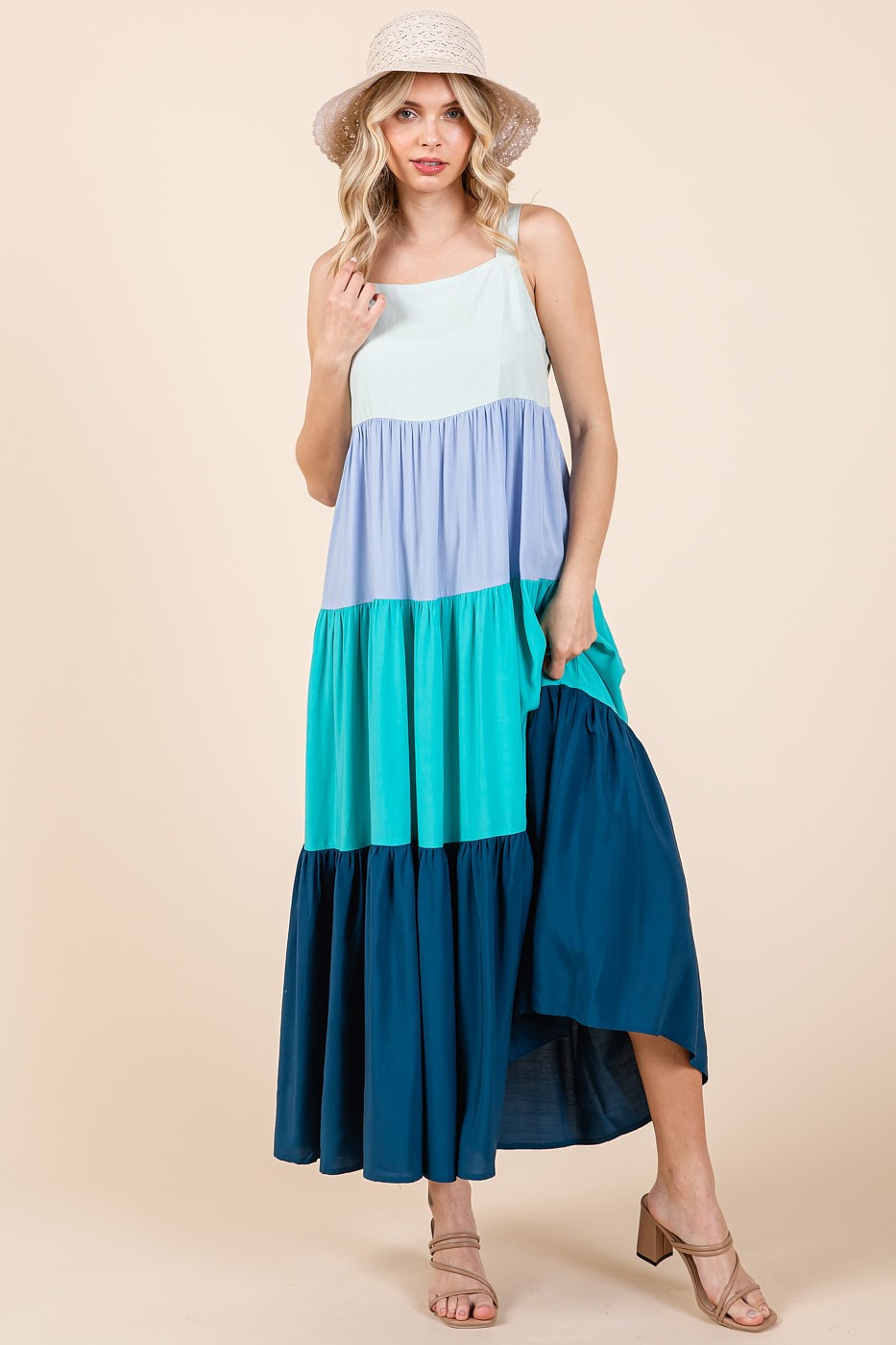 woman wearing a color-blocked maxi dress with light blue, teal, and navy panels, paired with a straw hat and sandals