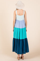 woman wearing a multicolored tiered maxi dress in shades of blue and green, with a wide-brimmed hat
